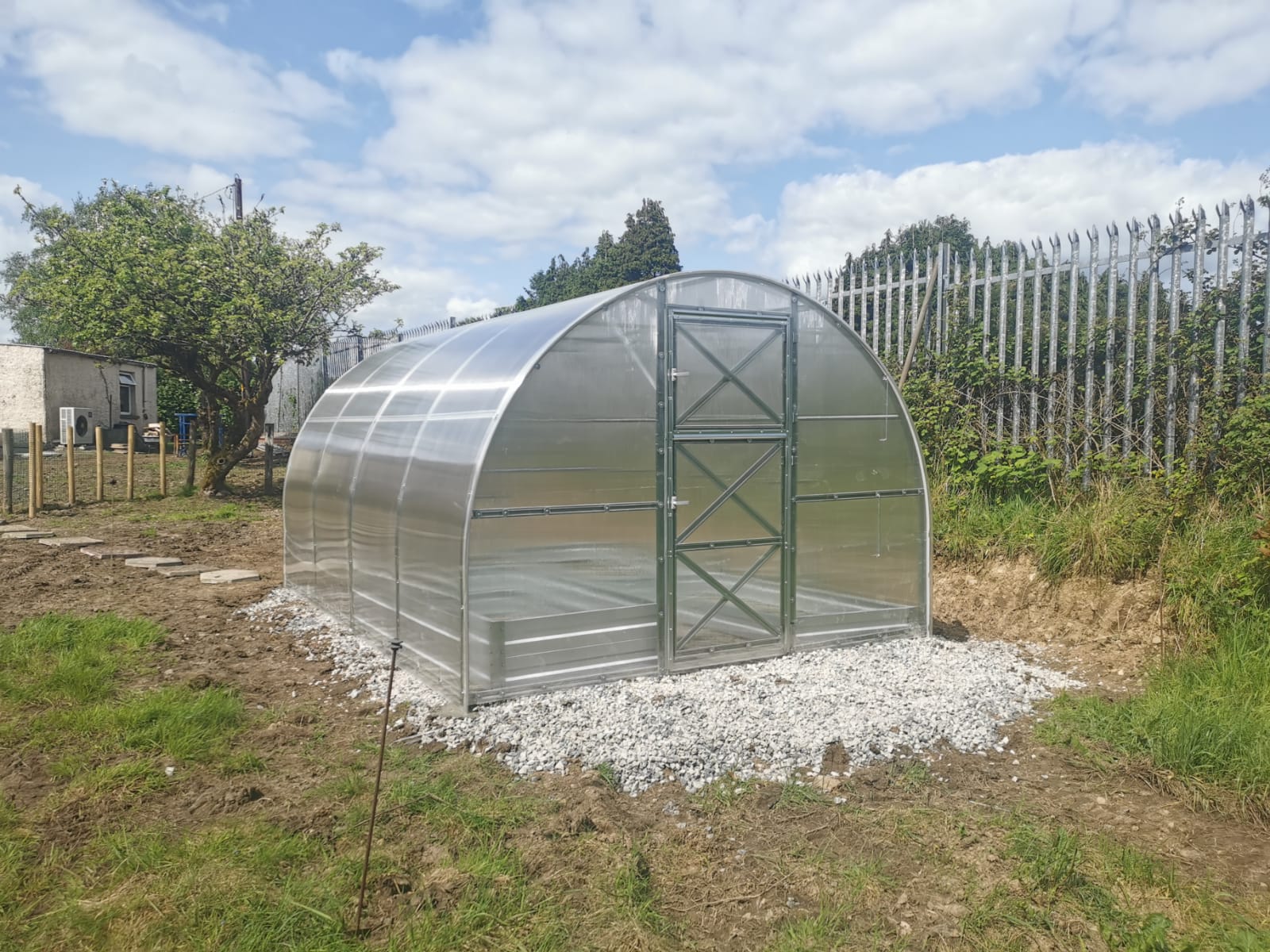 Arch-style greenhouse with 4mm polycarbonate panels on gravel foundation in backyard