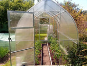 Barn-style polycarbonate greenhouse with open door showing tomato plants growing in soil beds