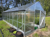 Gable-style polycarbonate greenhouse with galvanized frame showing ventilation window and plants growing inside