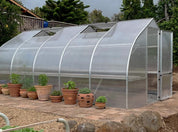Large polycarbonate greenhouse with multiple roof vents on brick patio with potted herbs