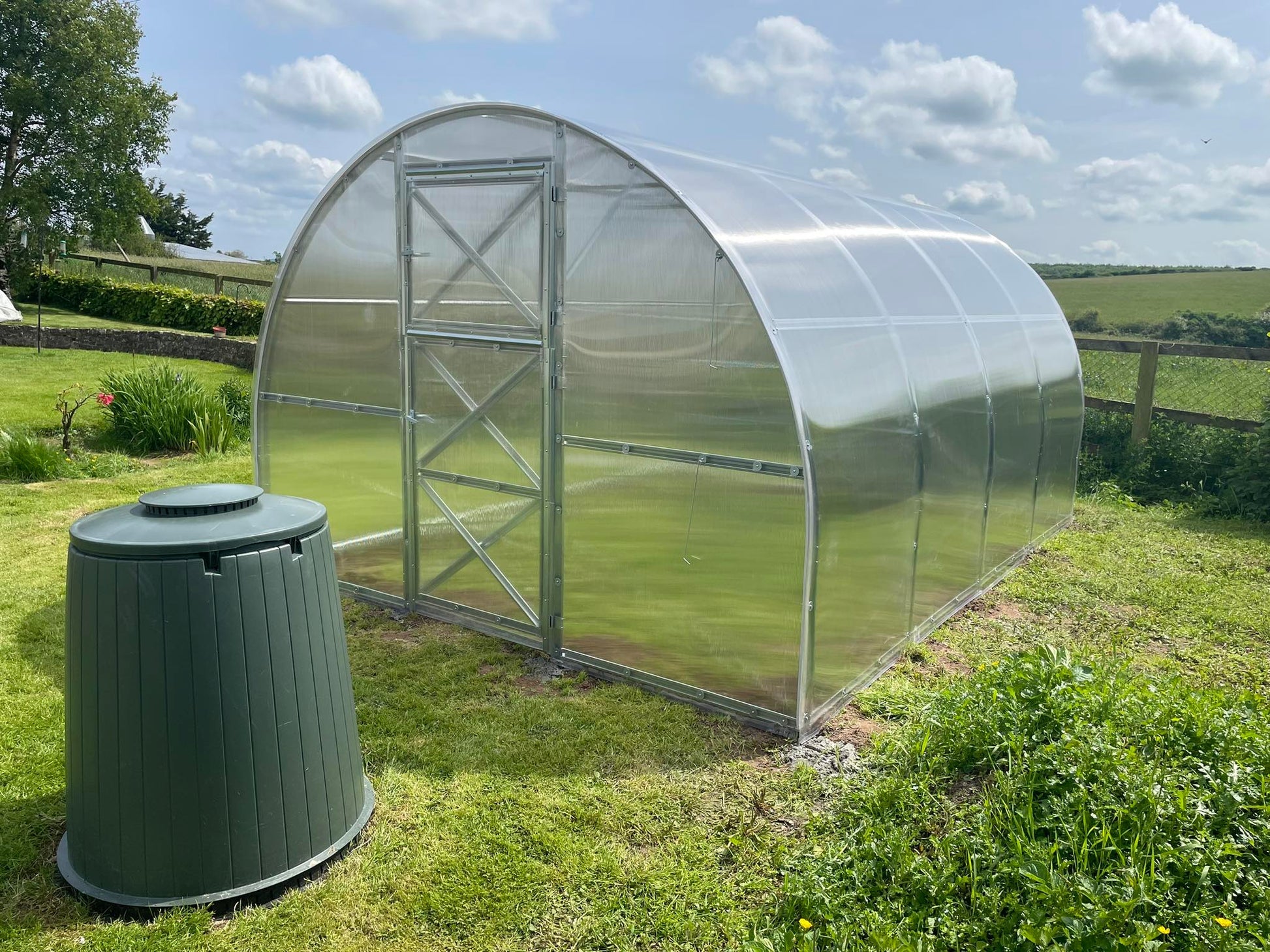 Arch-style polycarbonate greenhouse on grass lawn in rural countryside setting