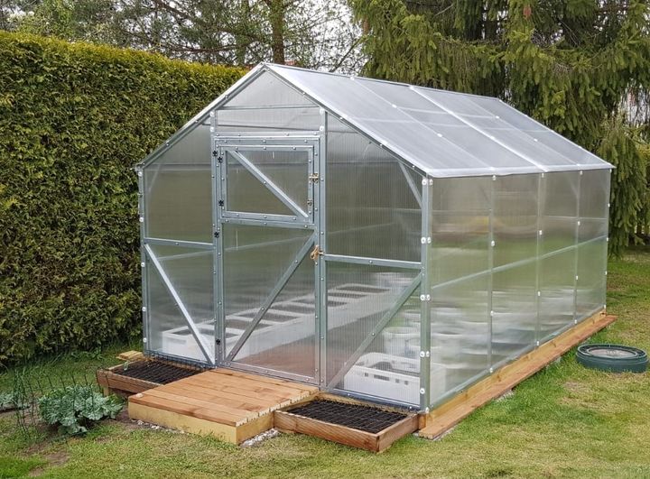 Gable-style polycarbonate greenhouse with galvanized steel frame on wooden deck with raised garden beds